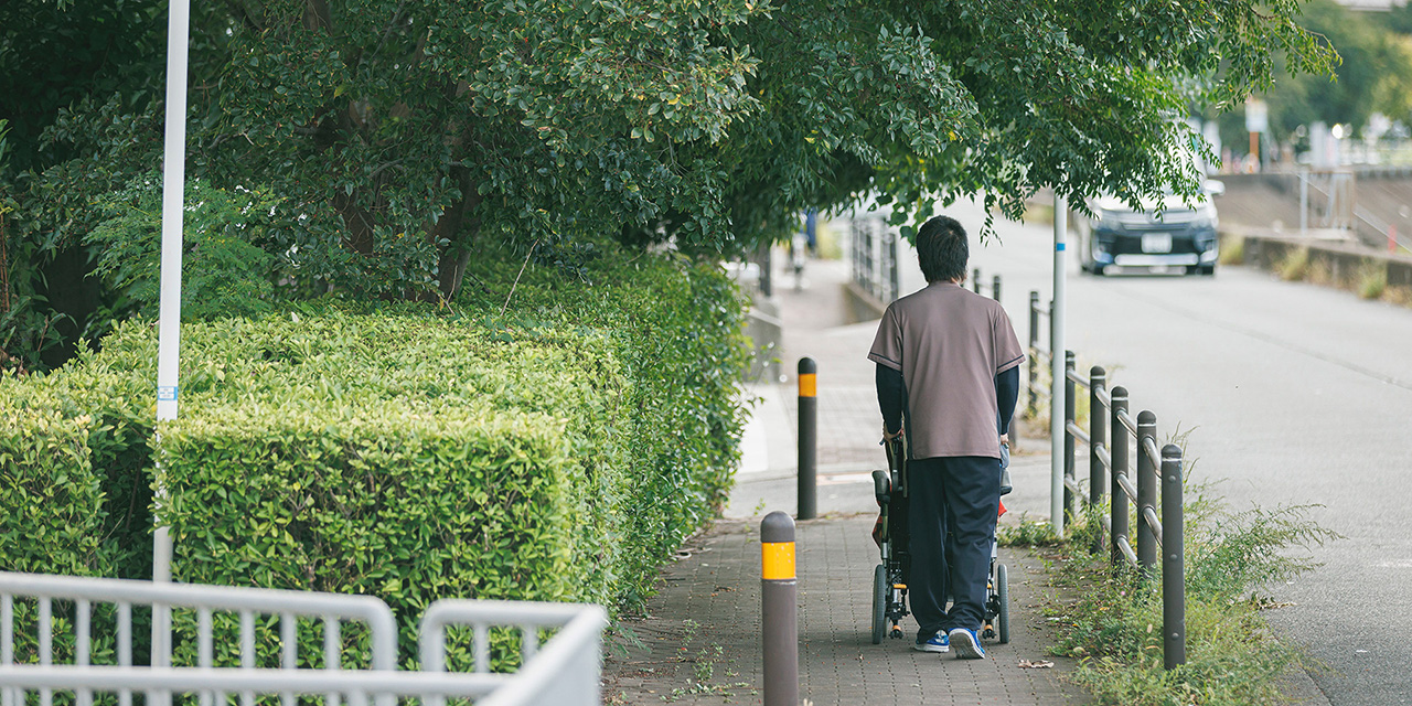 近隣の公園を散歩する車椅子の入居者と男性看護師